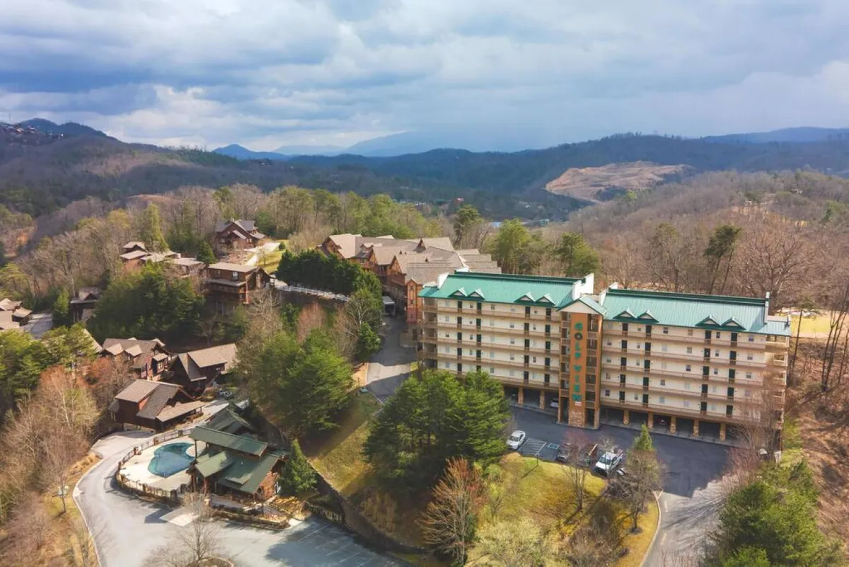 A welcoming view of a multi-story condo building surrounded by cabins, with a lush green landscape and ample parking area. The image captures the inviting exterior and the calm, family-friendly environment close to nature and local attractions.
