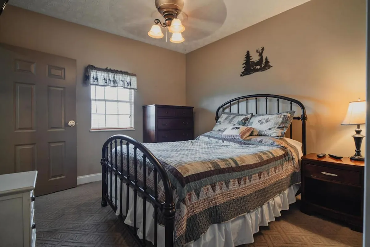 This image features a bed adorned with patterned bedding, a nightstand with a lamp, and a window with curtains letting in gentle sunlight. The atmosphere is cozy, welcoming, and ideal for winding down at the end of the day.