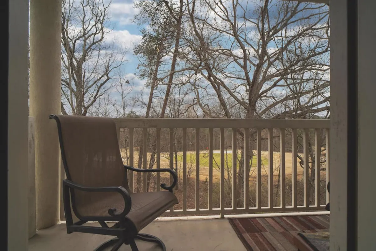 A peaceful private balcony with a single chair, a rug, and a view of lush trees. The setting is tranquil, ideal for enjoying a quiet morning coffee or sharing a special moment with a loved one while surrounded by nature.