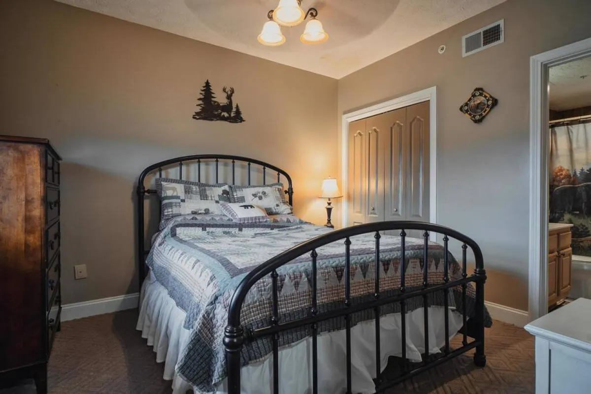 The room showcases a bed, a nightstand with a lamp, a wooden dresser, and tasteful wall decor. The space feels calm, tidy, and designed for restful solitude.