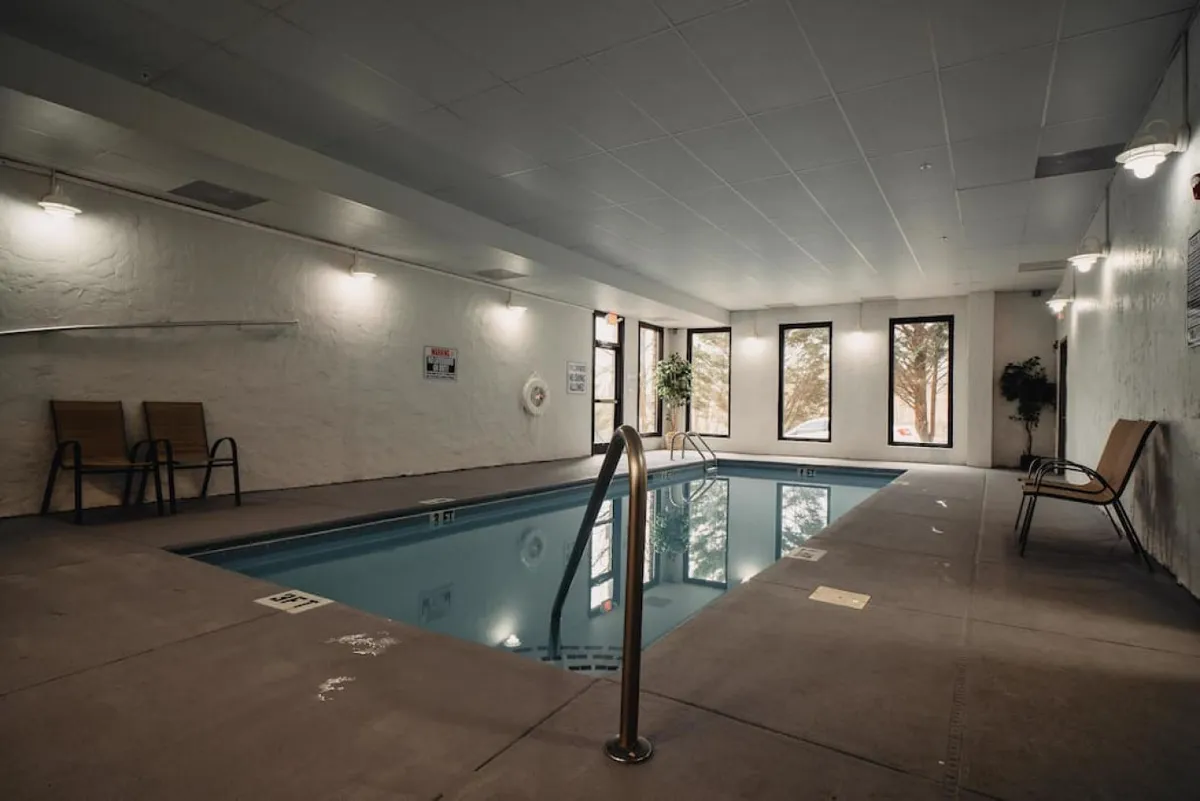 This image showcases a serene indoor pool area, with large windows letting in soft natural light, lounge chairs positioned for relaxation, and a tranquil atmosphere that invites guests to unwind and enjoy a refreshing swim. The view outside connects the interior to the lush surroundings.