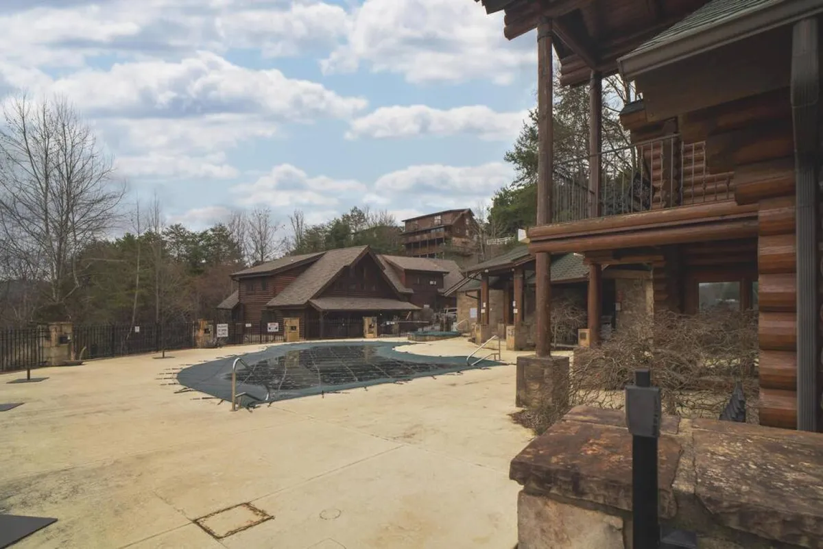 An inviting outdoor swimming pool set against a backdrop of log cabin architecture and lush greenery. The pool area is surrounded by peaceful nature, encouraging both relaxation and social gatherings in the open air.