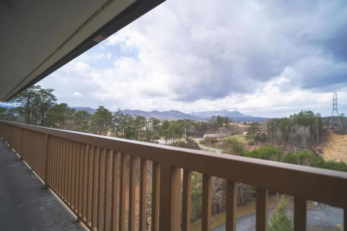 From a balcony vantage point, this image showcases a tranquil view of the mountain range, framed by trees and a balcony railing, inviting guests to enjoy peaceful mornings or relaxing evenings surrounded by nature.