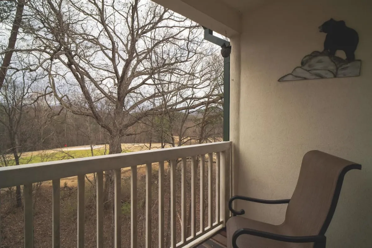 A serene balcony scene with a chair next to a bear decoration, leafy branches, and a view over the road. The balcony is inviting for morning coffee, reading, or taking in tranquil resort views.