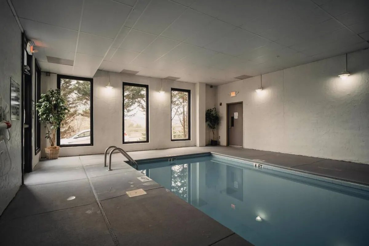 Inside a bright and airy resort indoor pool area, large windows let sunlight flood the space, highlighting the pool, potted plants, and poolside seating. The area is designed for relaxation and group enjoyment after days spent exploring local attractions.